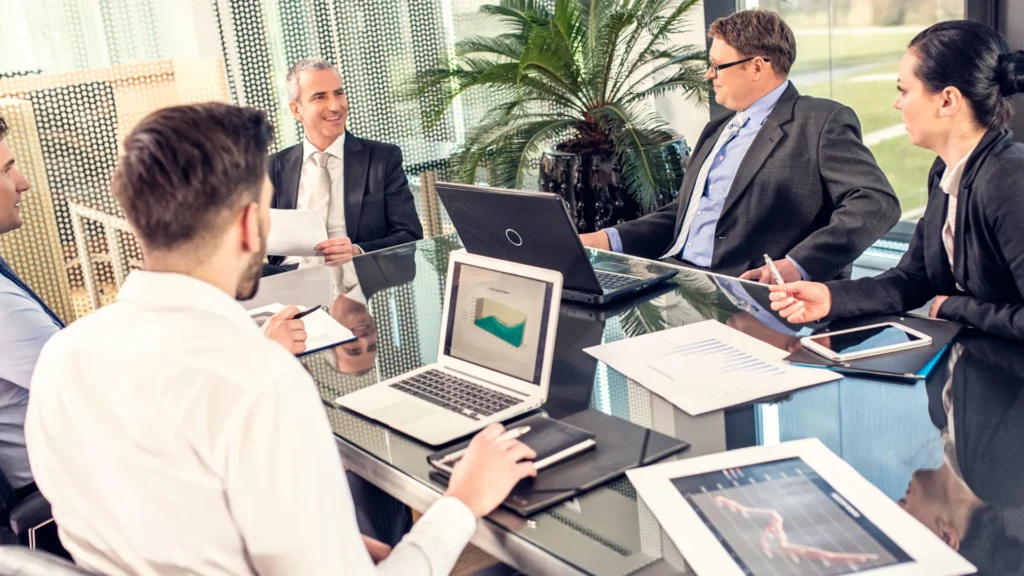 A group of professionals in a meeting discussing business strategies with laptops and documents